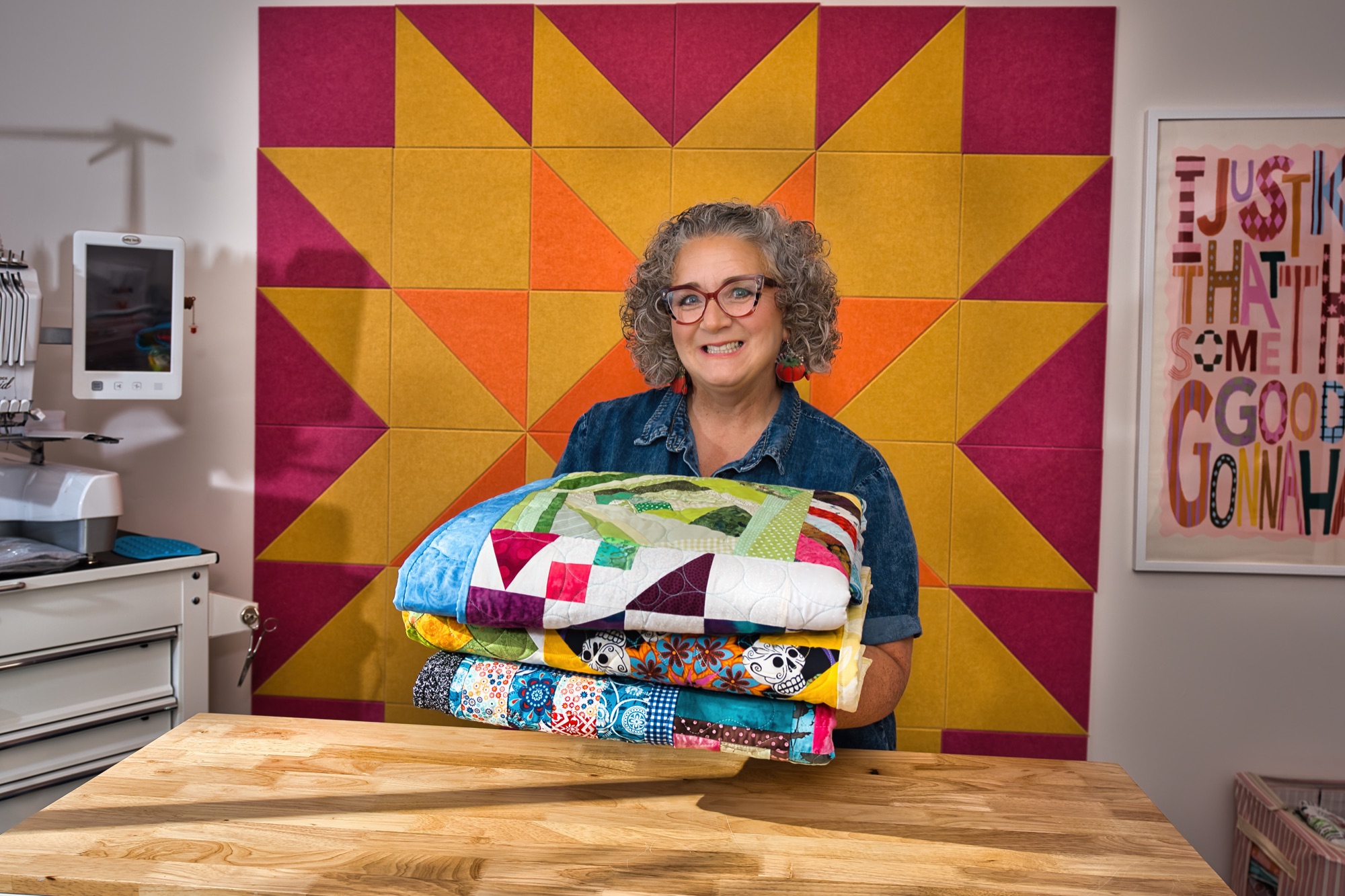 Angela holding a stack of quilts in front of the quilt-block wall in her she shed