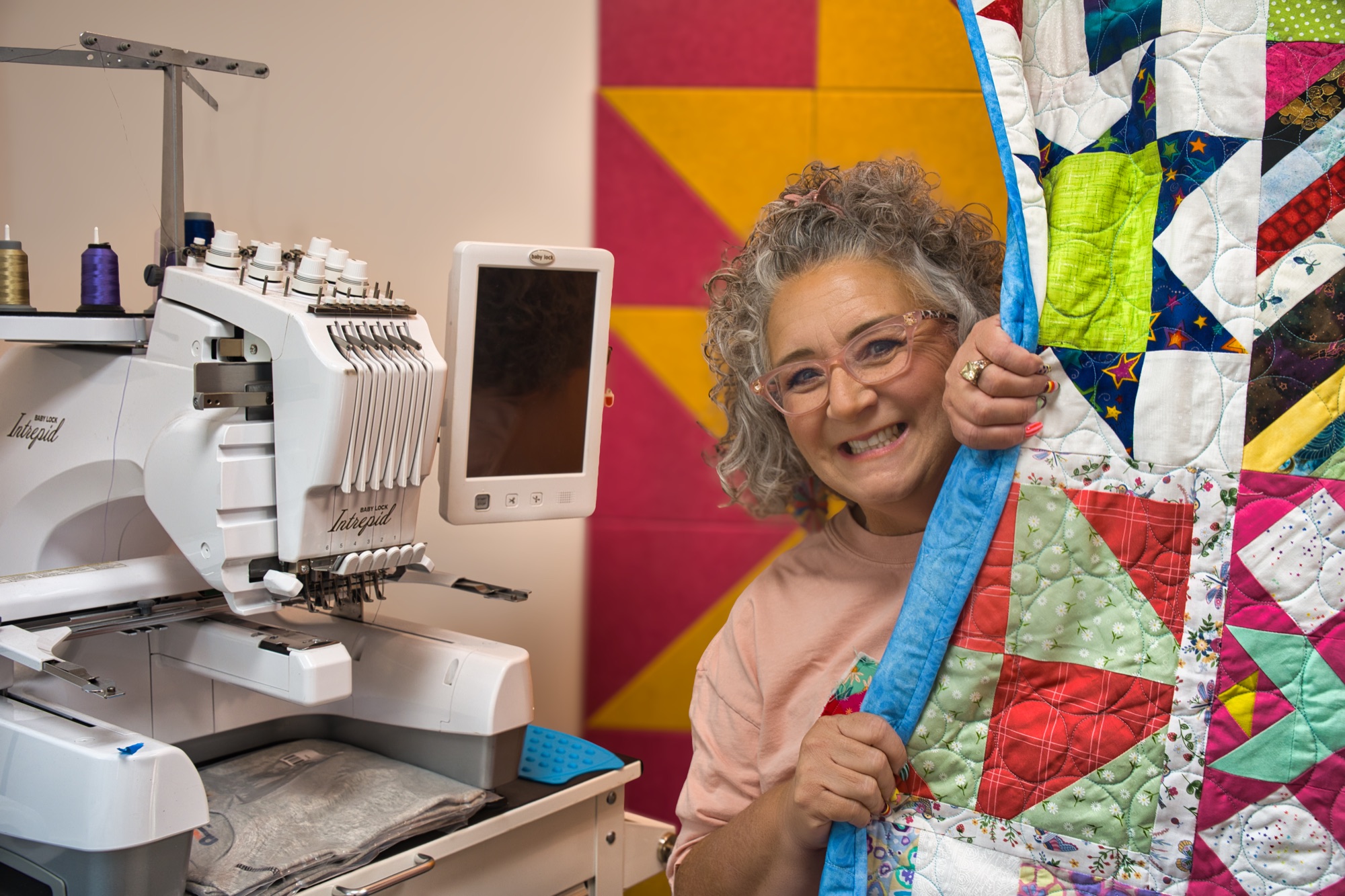 Angela holding up a finished patchwork quilt in front of the quilt-star wall