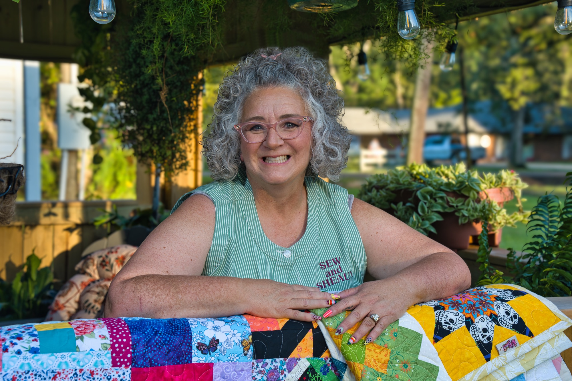 Angela smiling, leaning on a bright patchwork quilt under string lights at dusk